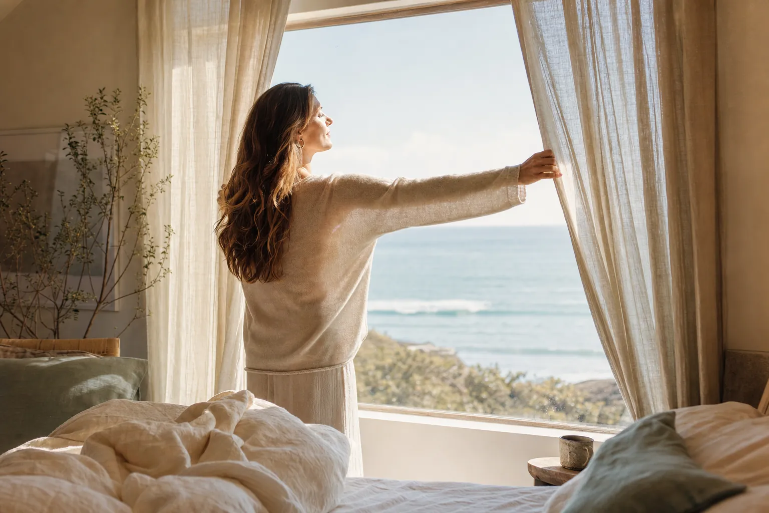 A woman opening sheer curtains to soft morning light