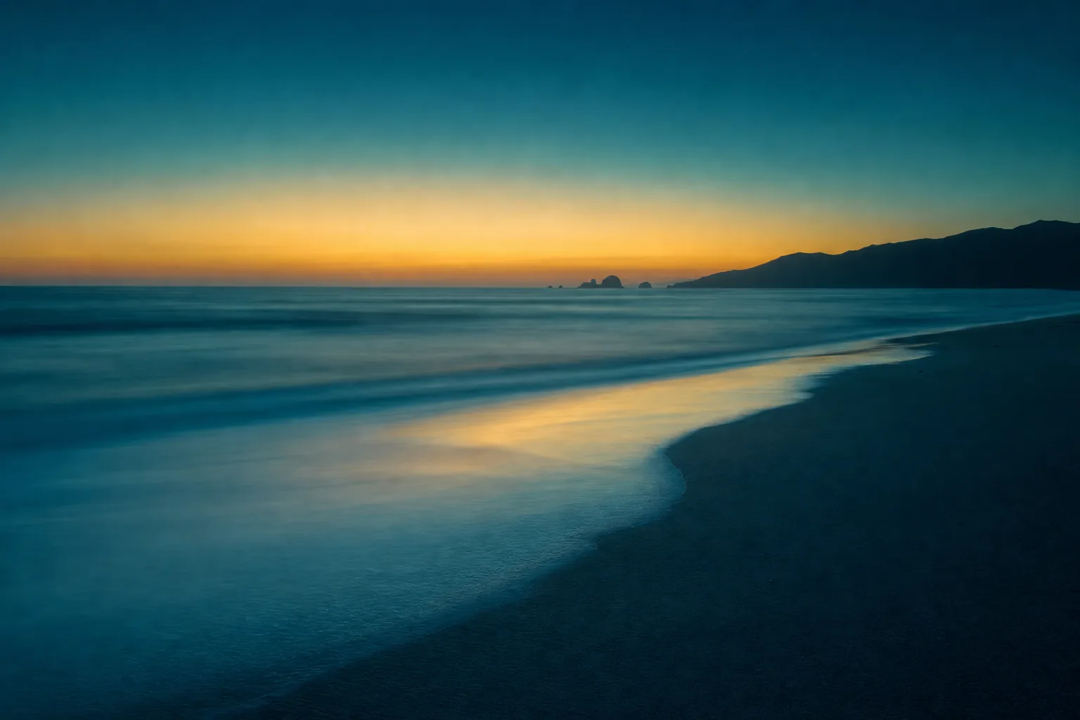 Ocean shoreline at dusk beneath a gold horizon